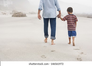 Rear view of father and son holding hands while walking on sand at beach