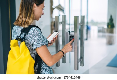 Rear view of female 20s with backpack standing near door use mobile phone with mock up screen for entering security code unlock electronic system,woman pressing key for entering holding mobile phone