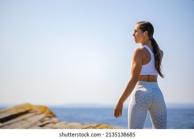 Rear View Of Female Athlete Resting After Workout Against Clear Sky And Sea On Sunny Day