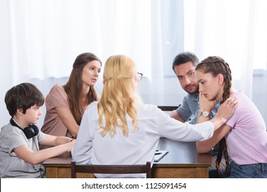 rear view of female counselor cheering up upset teenage girl on family therapy session in office 
