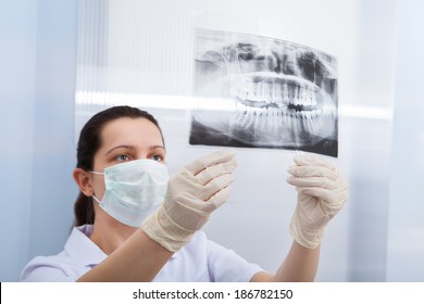 Rear View Of Female Dentist Looking At Dental Xray In Clinic