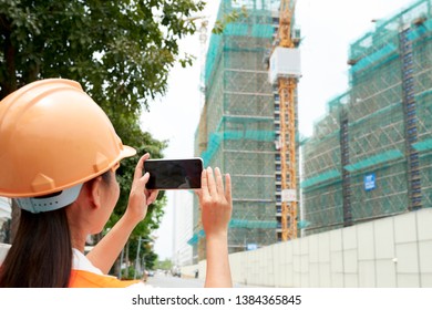 Rear View Of Female Engineer In Helmet Shooting A Video Or Making A Photo Of Building On Her Mobile Phone Outdoors