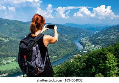 Rucksack mit Rucksack auf dem Berggipfel mit Blick auf den Tag und Fotografieren der Landschaft per Telefon.