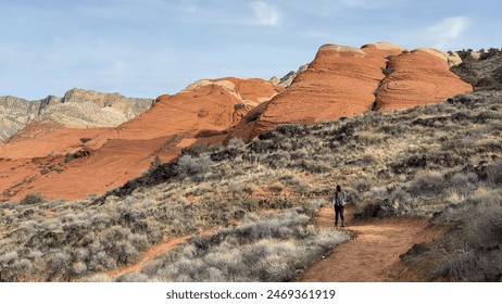 Rear view of a female hiker on a hiking trail winding in front of beautiful, orange colored petrified sand dunes in the desert - Snow Canyon State Park, St George, Utah, USA - Powered by Shutterstock