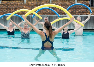 Rear view of female Instructor and senior swimmers exercising with pool noodle - Powered by Shutterstock
