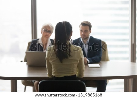 Rear view of female job applicant talking to recruiters listen at job interview, woman vacancy candidate seeker sits back making first impression on hr managers in office, hiring recruitment concept
