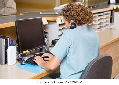Rear View Of Female Nurse Answering Telephone While Working On Computer At Hospital Reception