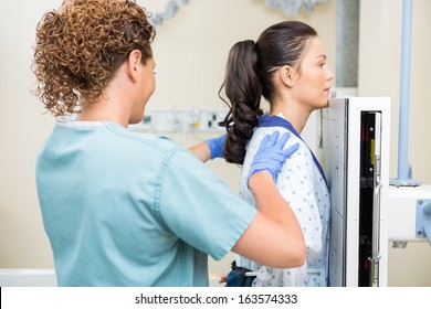 Rear View Of Female Nurse Preparing Patient For Chest Xray In Examination Room