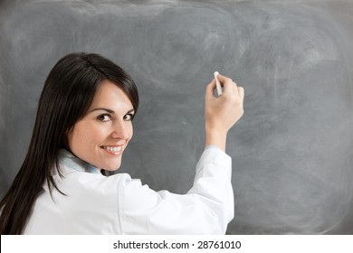 rear view of female teacher in lab clothes holding chalk against blank blackboard. Copy space - Powered by Shutterstock