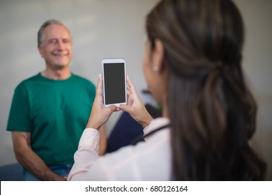 Rear view of female therapist photographing senior male patient from mobile phone at hospital ward - Powered by Shutterstock