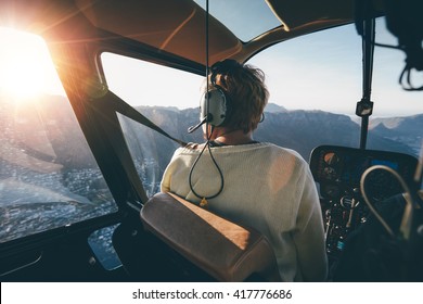 Rear view of female tourist on helicopter looking out of the window. Helicopter passenger admiring the view.