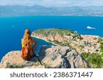 Rear view of female tourist sitting and looking at town of Nafplio city from Palamidi castle in Peloponnese. Greece