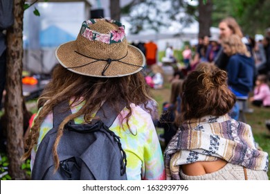 Rear View Of Female Wearing Wicker Sun Hat By Friend Against Audience Listening Fairytale Story. During Event In City At World And Spoken Word Festival