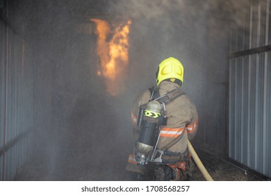 Rear View Of Fireman Wear Fire Protection Suit Walking Into The Training Room And Spray Water Fire At Fire Station. Training Fire Drill Concept.
