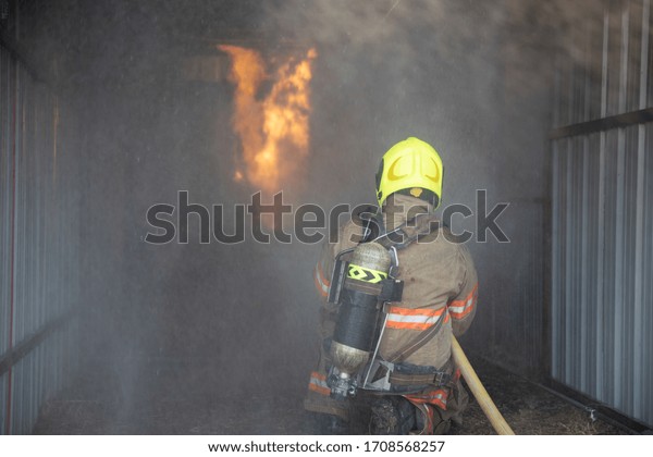 Rear view of Fireman wear fire protection suit\
walking into the training room and Spray water Fire at fire\
station. Training fire drill\
Concept.\
