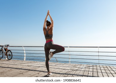 Rear View Of Fit And Healthy Woman Doing Yoga Exercises On A Pier, Looking At The Sea During Workout