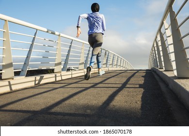 Rear view of fit mixed race woman wearing hijab and sportswear exercising outdoors in the city on a sunny day, running on a footbridge. Urban lifestyle exercise. - Powered by Shutterstock