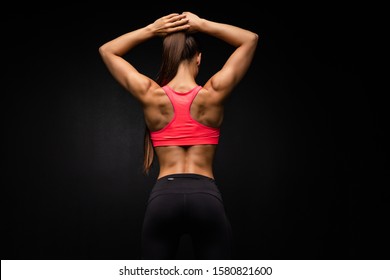 Rear view of a fit strong young woman with a muscular toned body wearing sportswear looking to the side, on grey with copy space
