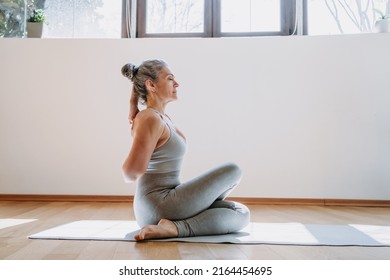 Rear view of fit woman doing gomukhasana at home. Fitness female holding hands behind back and stretching. Grey-haired senior lady is engaged in fitness, stretching, yoga - Shutterstock ID 2164454695