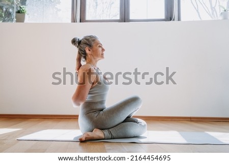 Rear view of fit woman doing gomukhasana at home. Fitness female holding hands behind back and stretching. Grey-haired senior lady is engaged in fitness, stretching, yoga Foto stock © 