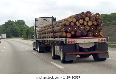 Rear View Of Flatbed Semi Truck Hauling A Cargo Of Telephone Poles.