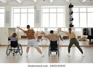 Rear view of four diverse men and women practicing dance with wheelchairs in front of mirrors in studio, long shot - Powered by Shutterstock