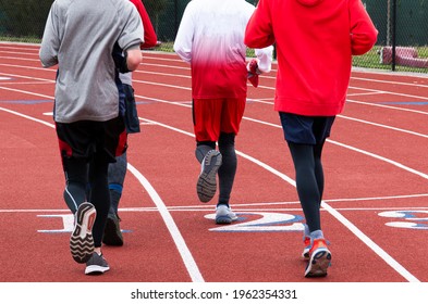 REar View Of Four High School Runners Running On A Track Crossing The Finish Line Together In A Group During Track And Field Pracice.