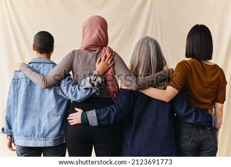 Rear view of four women with arms around each other in support of International Women's Day