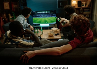 Rear view of four young male friends spending evening indoors watching soccer match on TV and drinking beer - Powered by Shutterstock