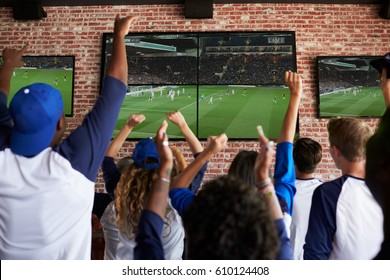 Rear View Of Friends Watching Game In Sports Bar Celebrating
