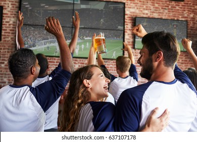 Rear View Of Friends Watching Game In Sports Bar On Screens