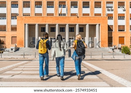 Rear view full length of three unrecognizable multi-ethnic students talking while walking along the campus