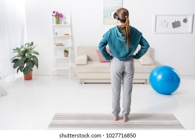 rear view of girl exercising with virtual reality headset at home