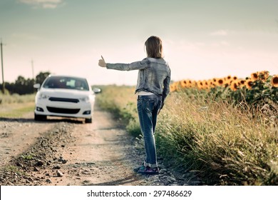 Rear View of a Girl Hitchhiking Along the Road While Showing Thumbs Up Gesture to a Car Passing by.