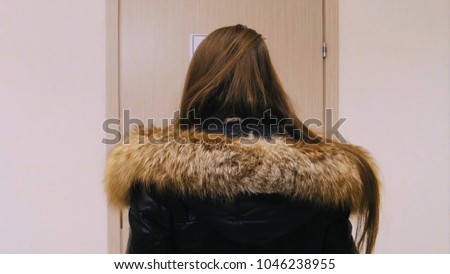 Rear view of the girl in the winter jacket standing opposite the door upset and angry. girl stands opposite the door of the office and does not understand why it is closed. Back view of woman thinking