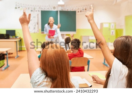 Rear view of girls raising hand while sitting on bench during lecture in classroom at school