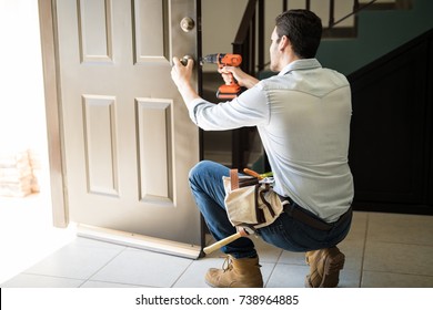 Rear view of a good looking man working as handyman and fixing a door lock in a house entrance