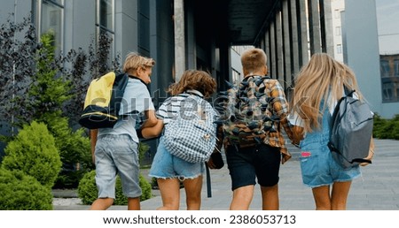 Rear view. Good-looking school child friends climb stairs going to class with backpacks. Boys and girls high school students having fun after school. They are smiling and having fun.
