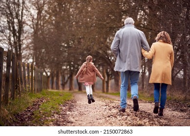 Rear View Of Grandparents With Granddaughter Outside Walking Through Winter Countryside