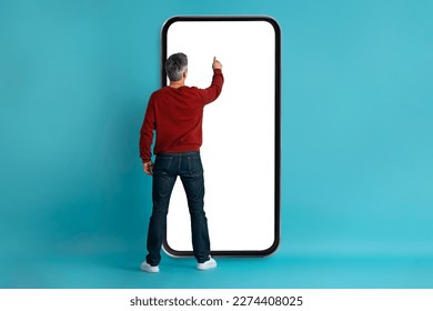 Rear view of grey-haired middle aged man in casual touching big phone white empty screen over blue studio background, checking newest mobile app, websurfing, mockup, copy space for ad - Shutterstock ID 2274408025