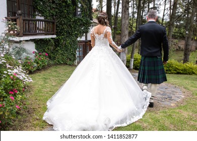 Rear View Of Groom And Bride Wearing Scottish Traditional Kilt And Bride In White Dress