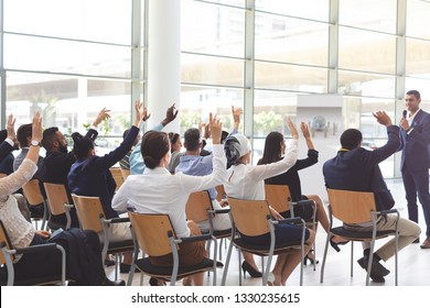 Rear view of group of diverse business people raising hands while listening to handsome mixed-race businessman at conference  - Powered by Shutterstock