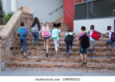 Rear View Of Group Of Diverse Students With Backpacks Climbing Up The Stairs Together At School. School And Education Concept