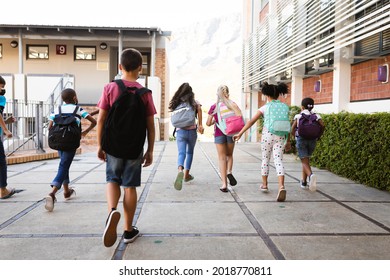 Rear View Of Group Of Diverse Students With Backpacks Running At Elementary School. Education Back To School Health Safety During Covid19 Coronavirus Pandemic.