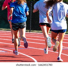 Rear View Of A Group Of High School Track Girls Running Together On A Red Track While Running Intervals.