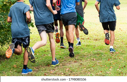 Rear View Of A Group Of High School Boys Training For Cross Country Running Grass In A Local Park.