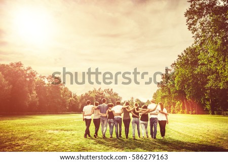 Rear view of group of Teenage Friends walking in the Park at Sunset
