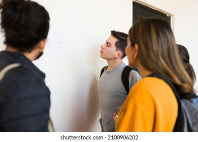 Rear View Of A Group Of Worried College Students Looking At The List With Their Final Grades 