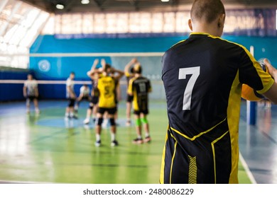 Rear view of guy volleyballist in sportswear uniform black yellow t-shirt with 7 number on back at volleyball game. Team match in sport school gym. Sports games, success concept. Copy ad text space - Powered by Shutterstock