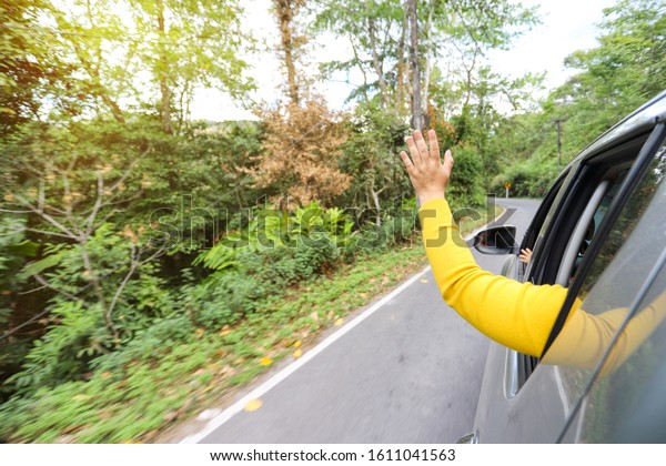 Rear view hand waving outside car during driving\
along beautiful nature\
view